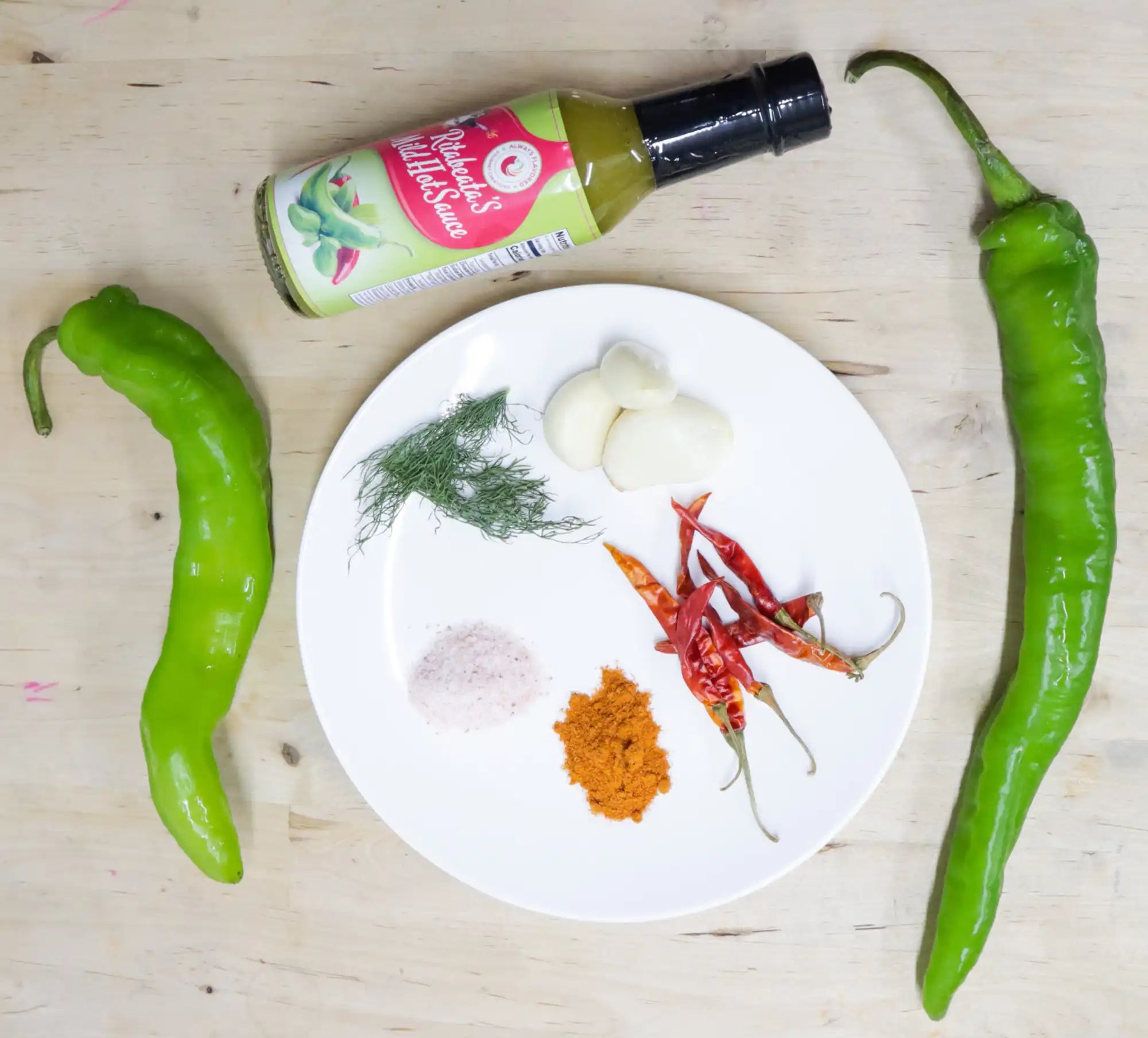 White plate containing spices, dried red chilies, and fresh dill alongside two green chili peppers and a sauce bottle.