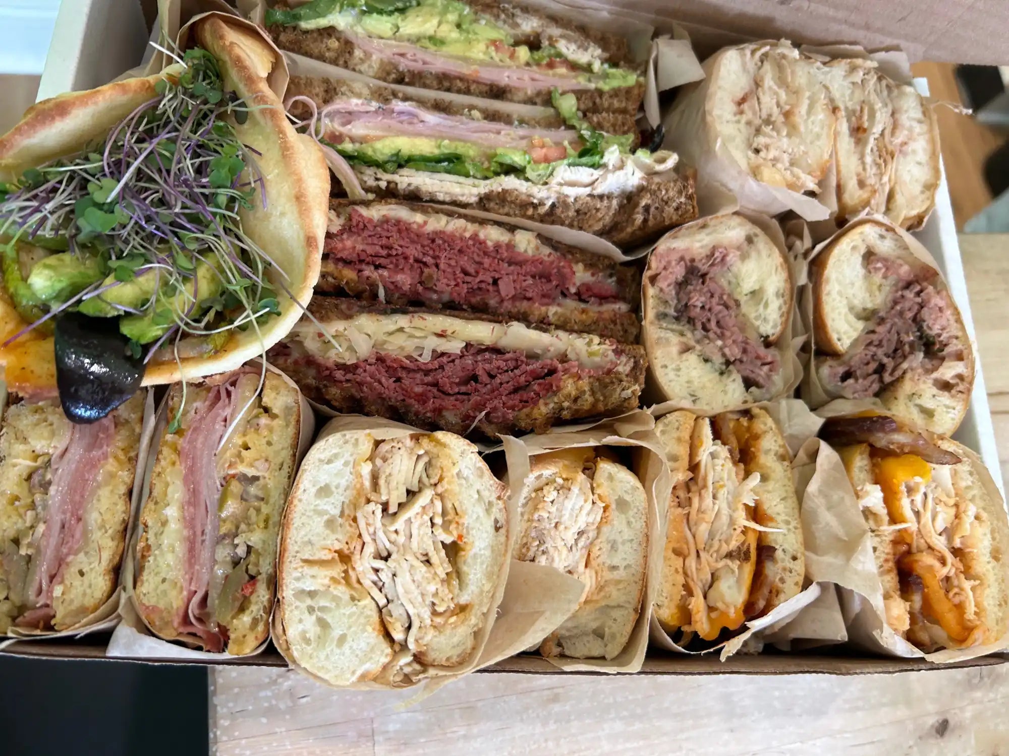 Collection of assorted deli sandwiches including pastrami, turkey, and roast beef varieties wrapped in paper.