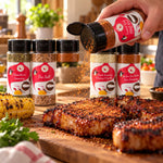 A hand holding a flavor first spice rack red and white shaker sprinkling tasty bbq seasoning on grilled pork chops