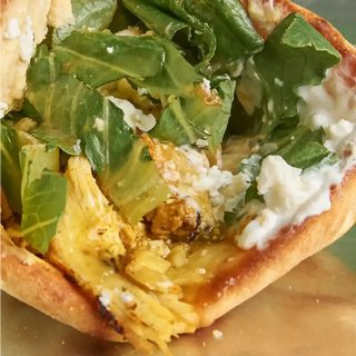 Sandwich filled with fresh greens, crumbled cheese, and yellow meat on a toasted bun.