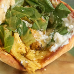 Sandwich filled with fresh greens, crumbled cheese, and yellow meat on a toasted bun.