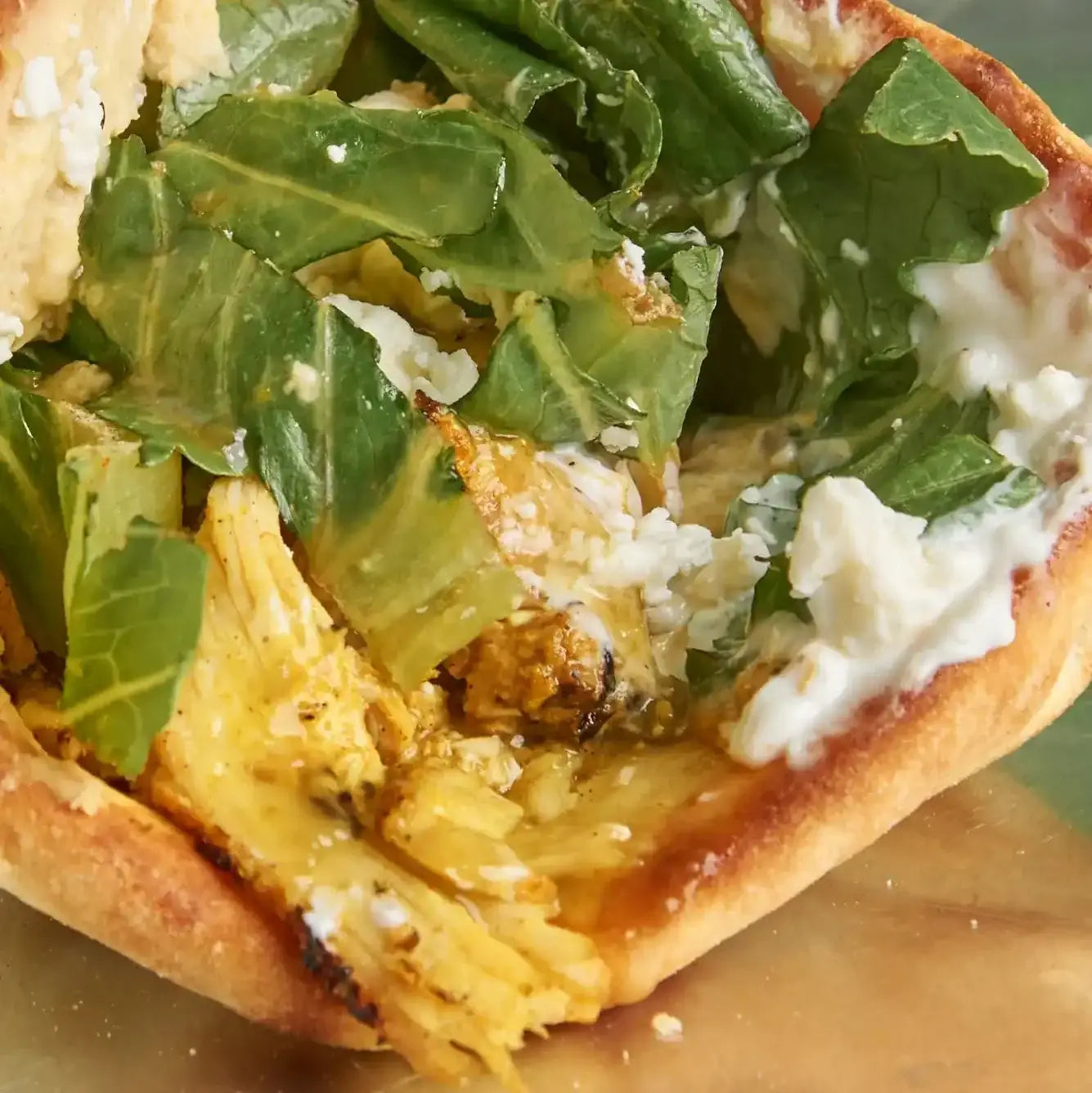Sandwich filled with fresh greens, crumbled cheese, and yellow meat on a toasted bun.
